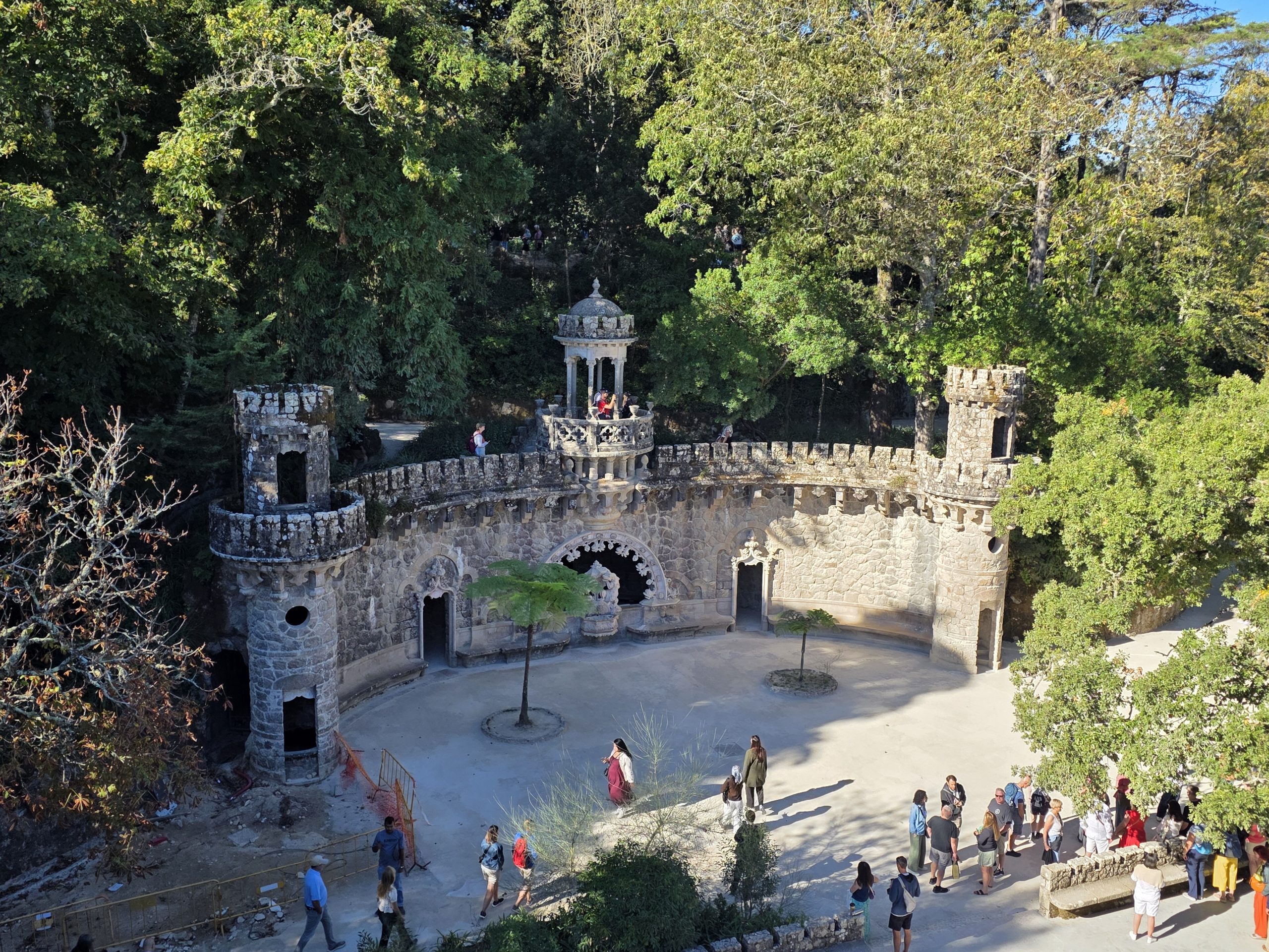 Curving stone terrace with two round turrets, an ornate central pavilion, and tree ferns.