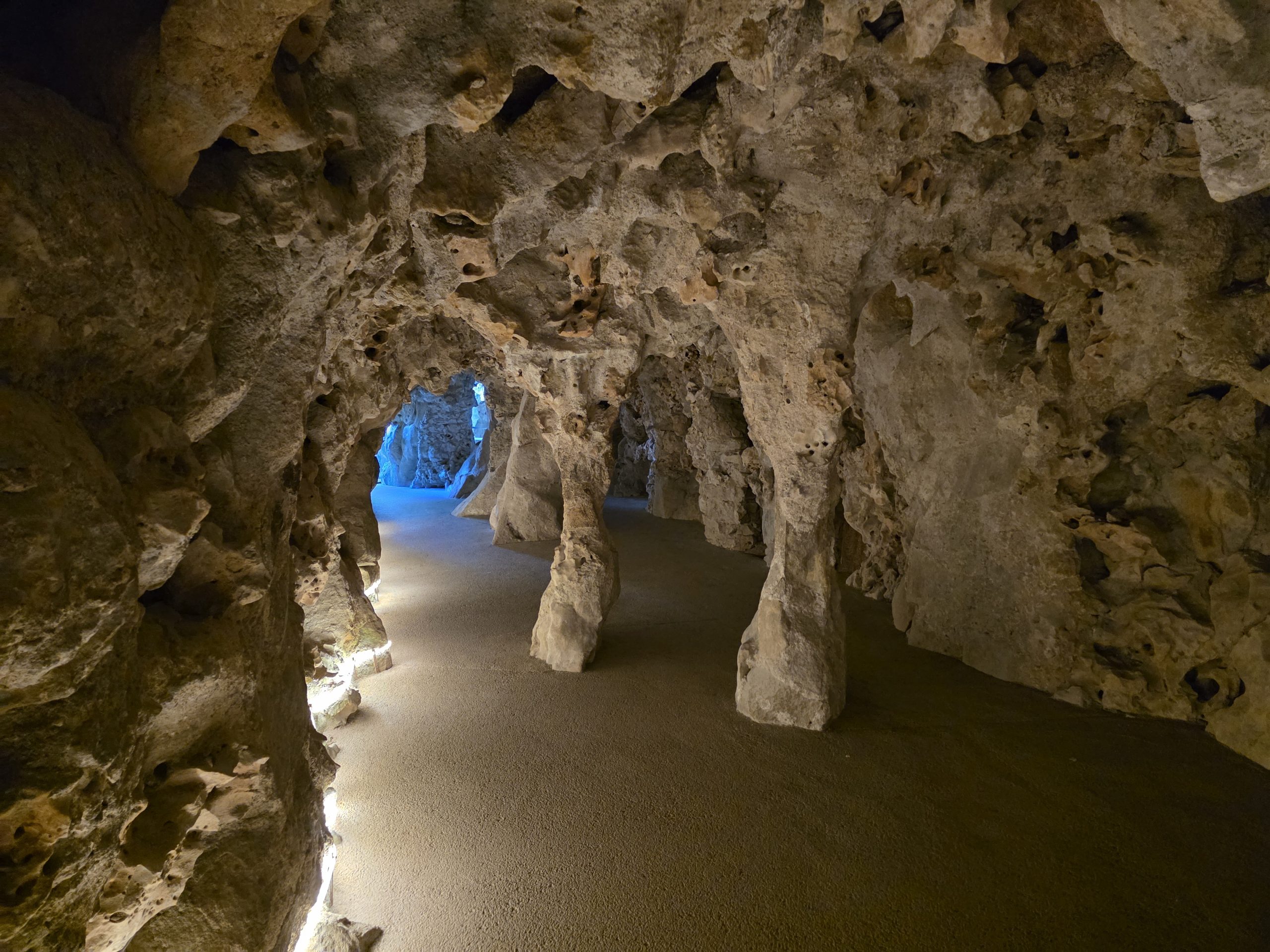 Rough stone columns and walls in an illuminated underground passage at Quinta da Regaleira.